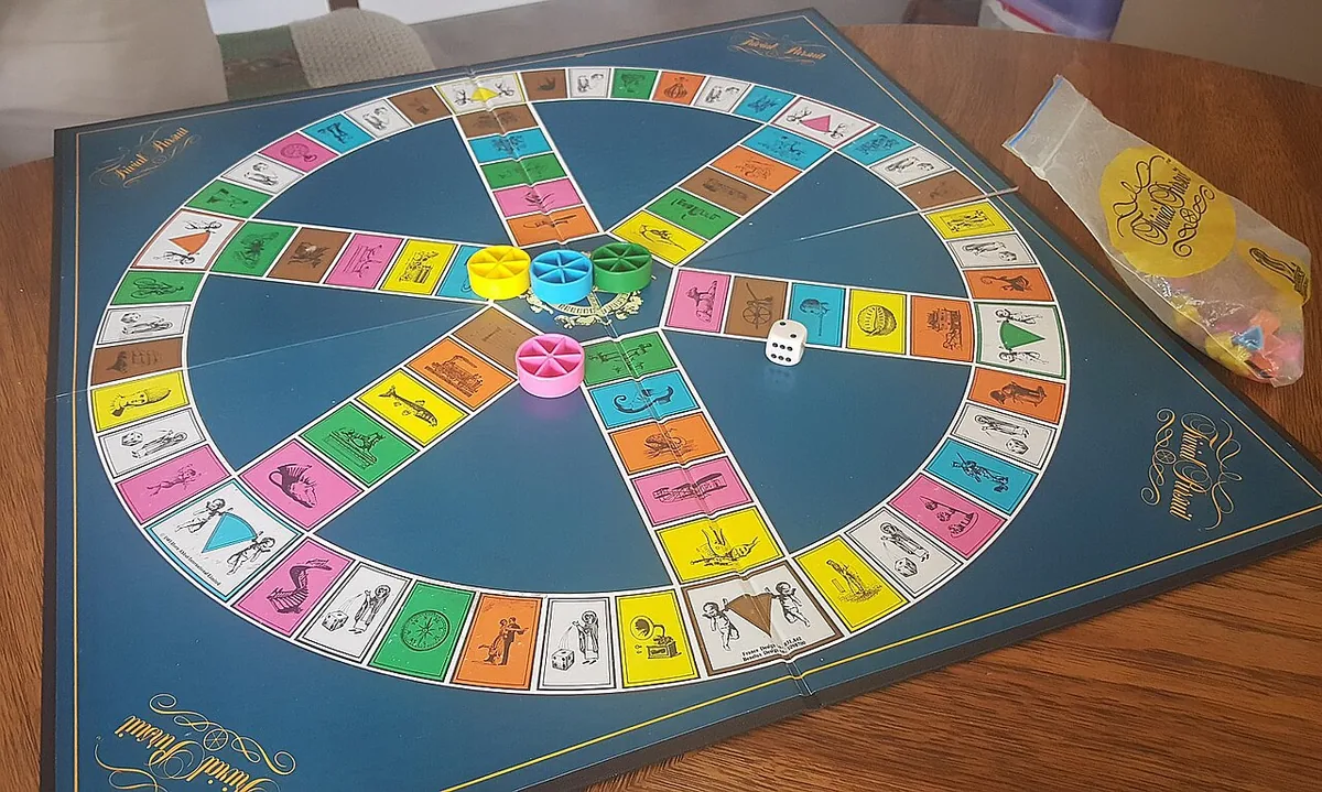 A vintage Trivial Pursuit board with its round track, coloured category wedge holders, a die and a bag of pieces